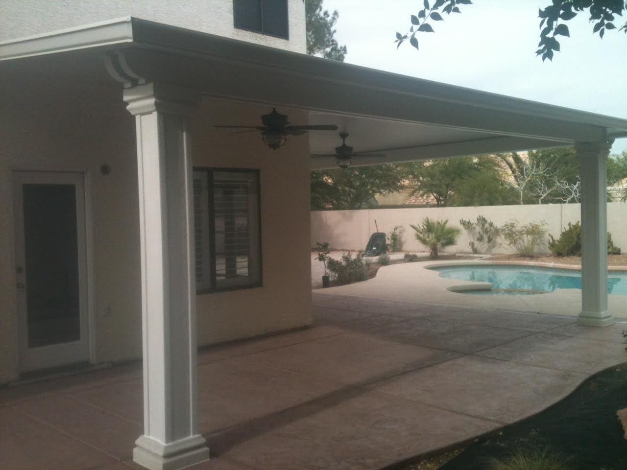 Solid patio cover with a fan beside a pool at dusk