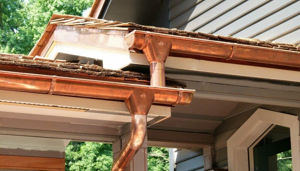 Seamless copper rain gutters and a round copper downspout on a cedar-shingle roofline